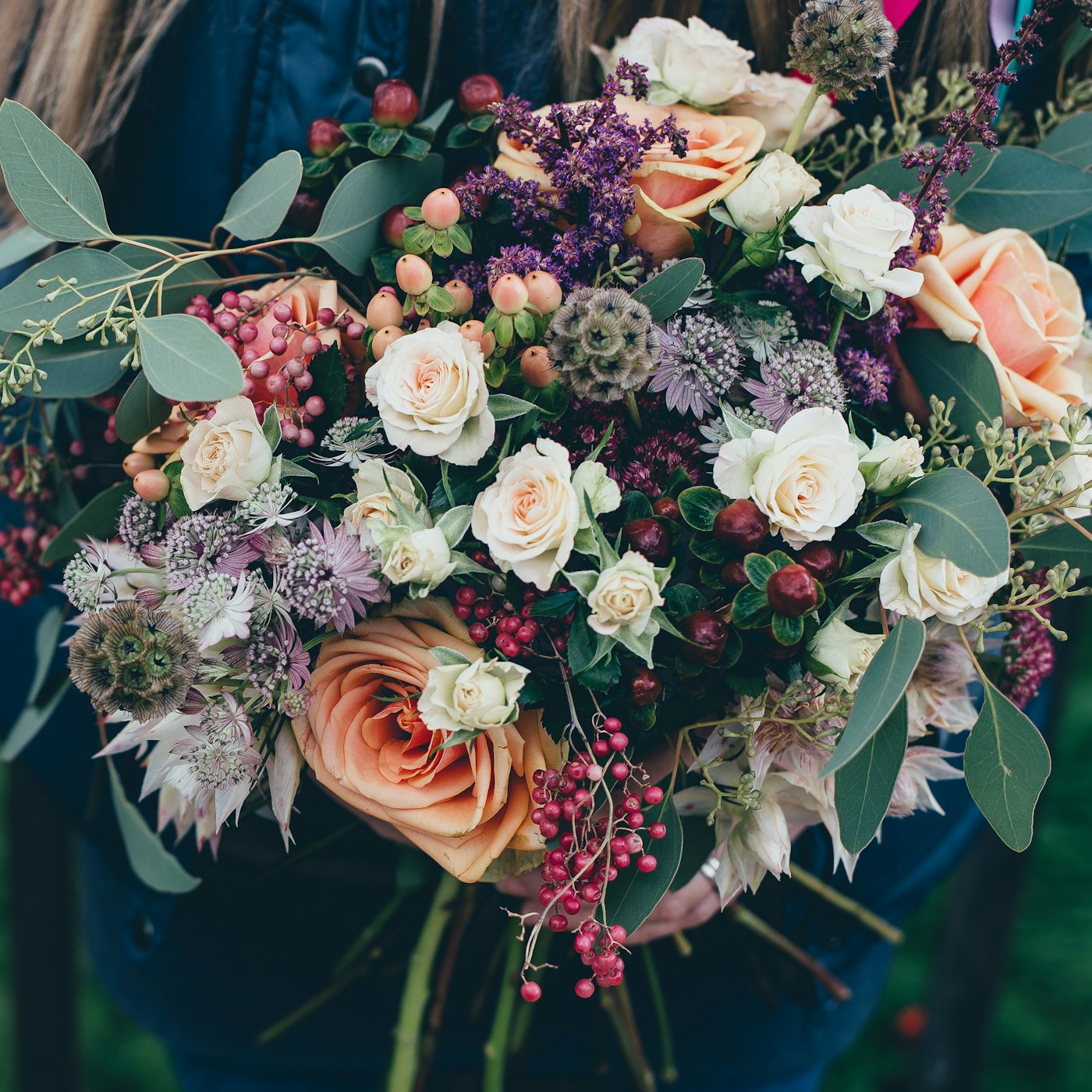 Bouquet composé de roses, d’eucalyptus et de baies, tenu à la main